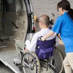 nurse helping patient in wheelchair into van-min