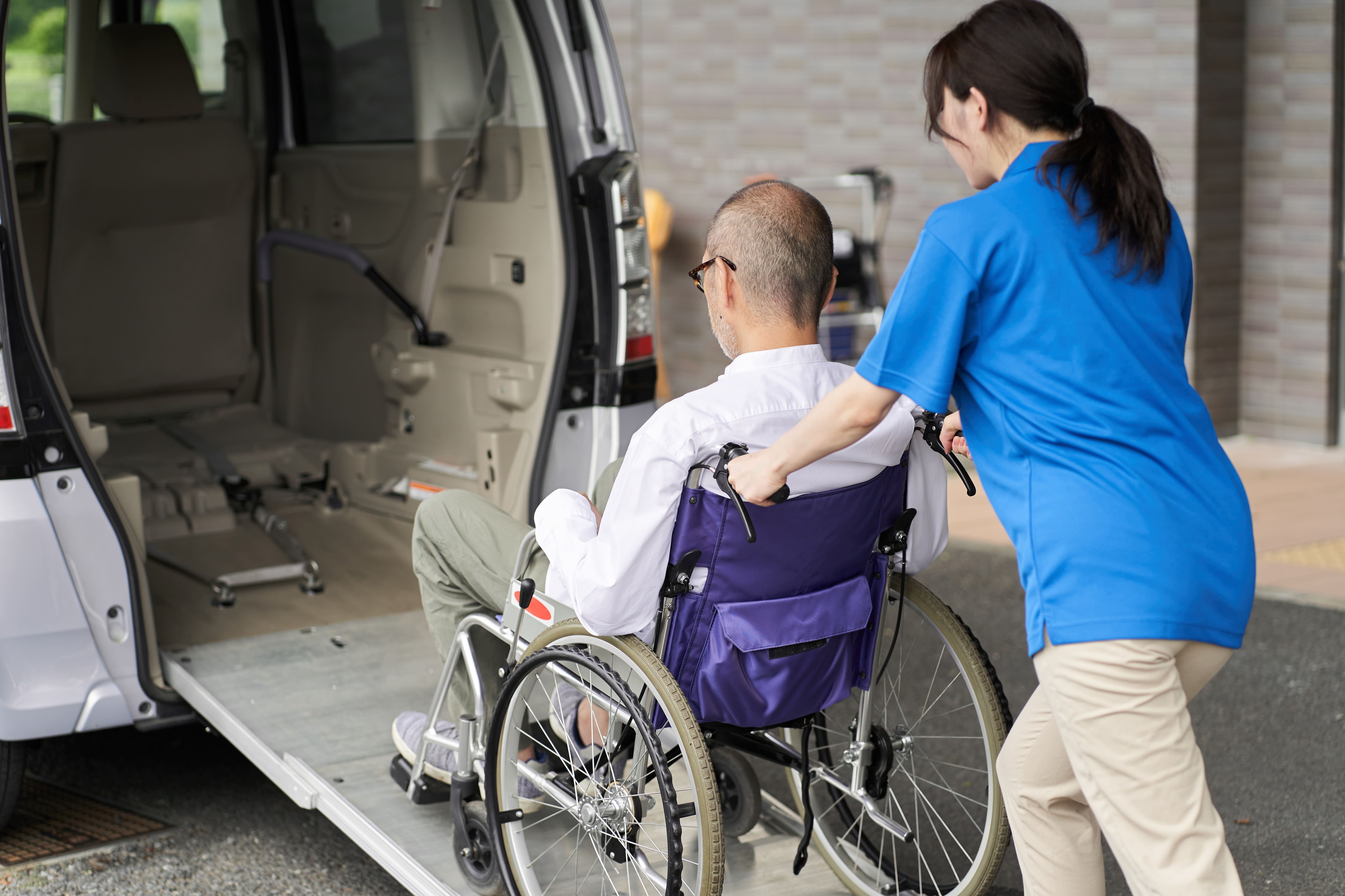 nurse helping patient in wheelchair into van-min